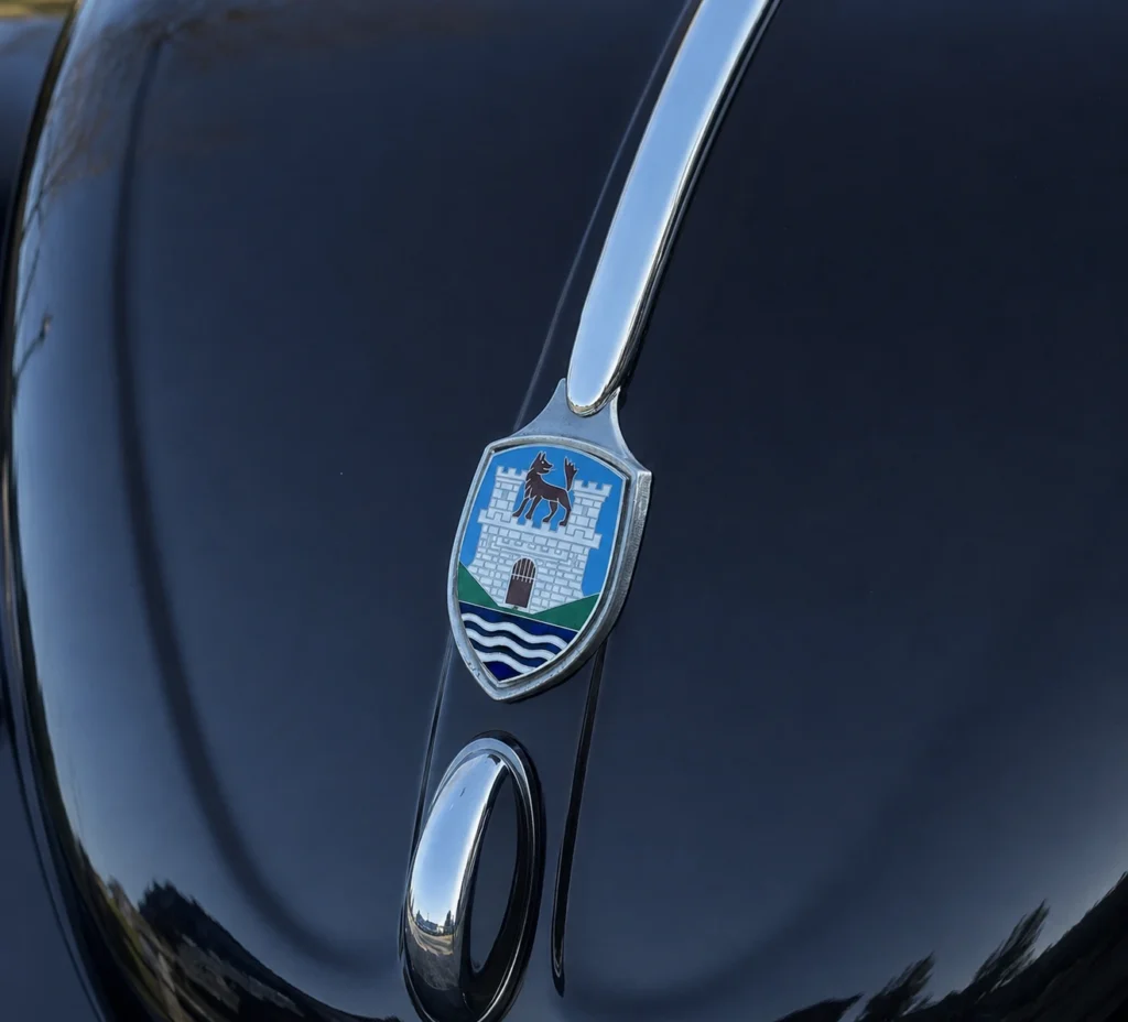 Volkswagen Coccinelle noire zoom sur son emblème de capot lié à la ville de Wolfburg
